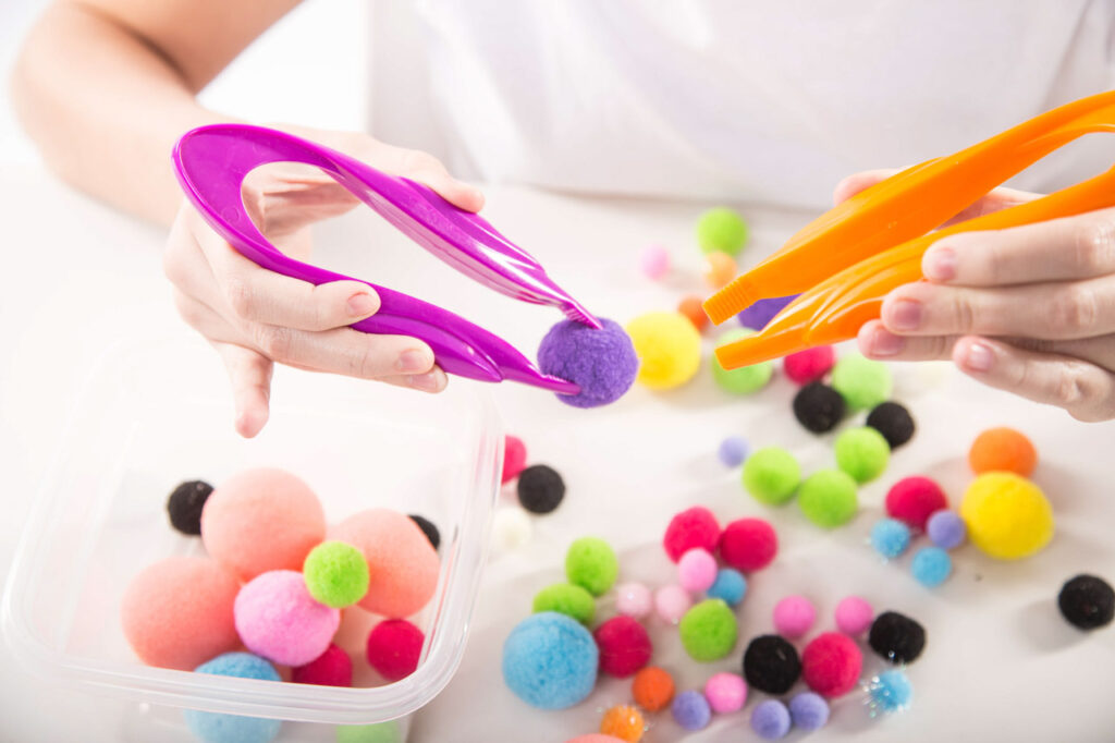 dziecięce rączki z pęsetami i kolorowymi pomponikami